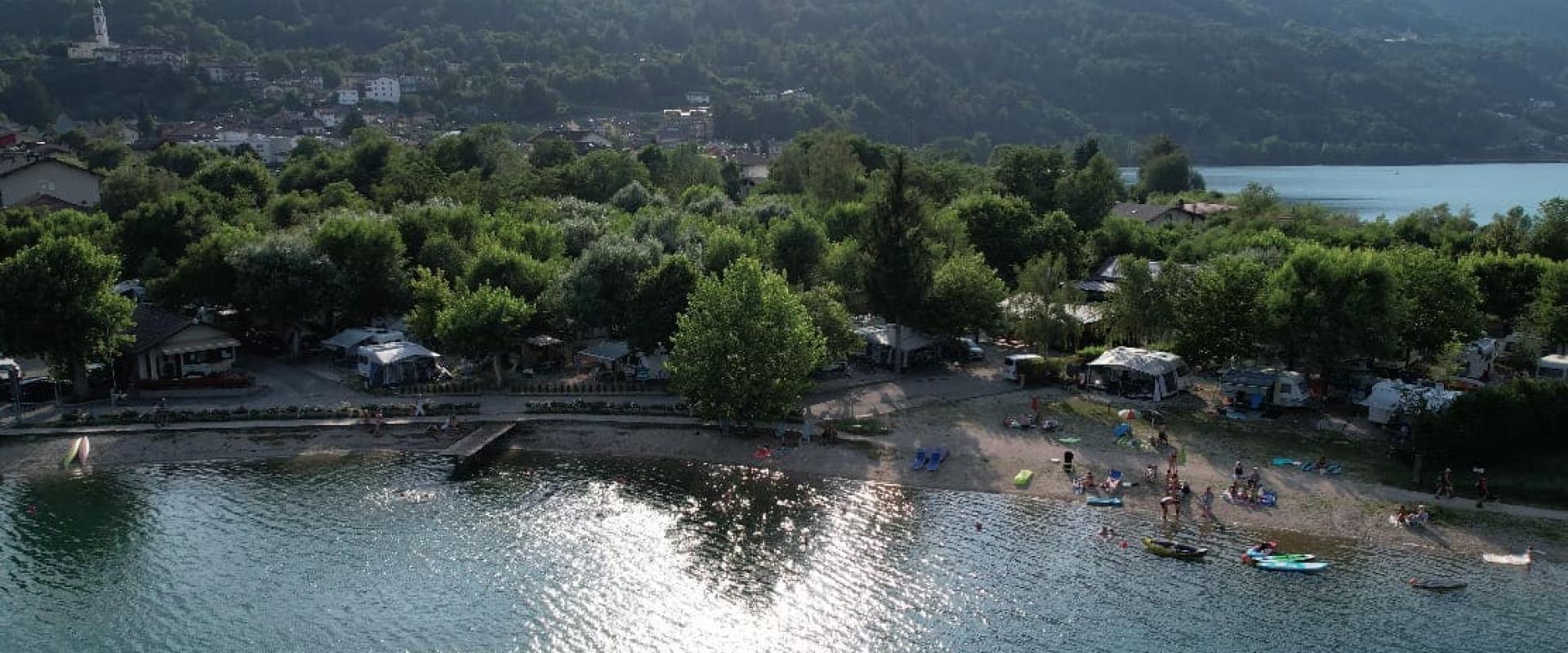 Spiaggia con persone e canoe, circondata da alberi e montagne sullo sfondo.