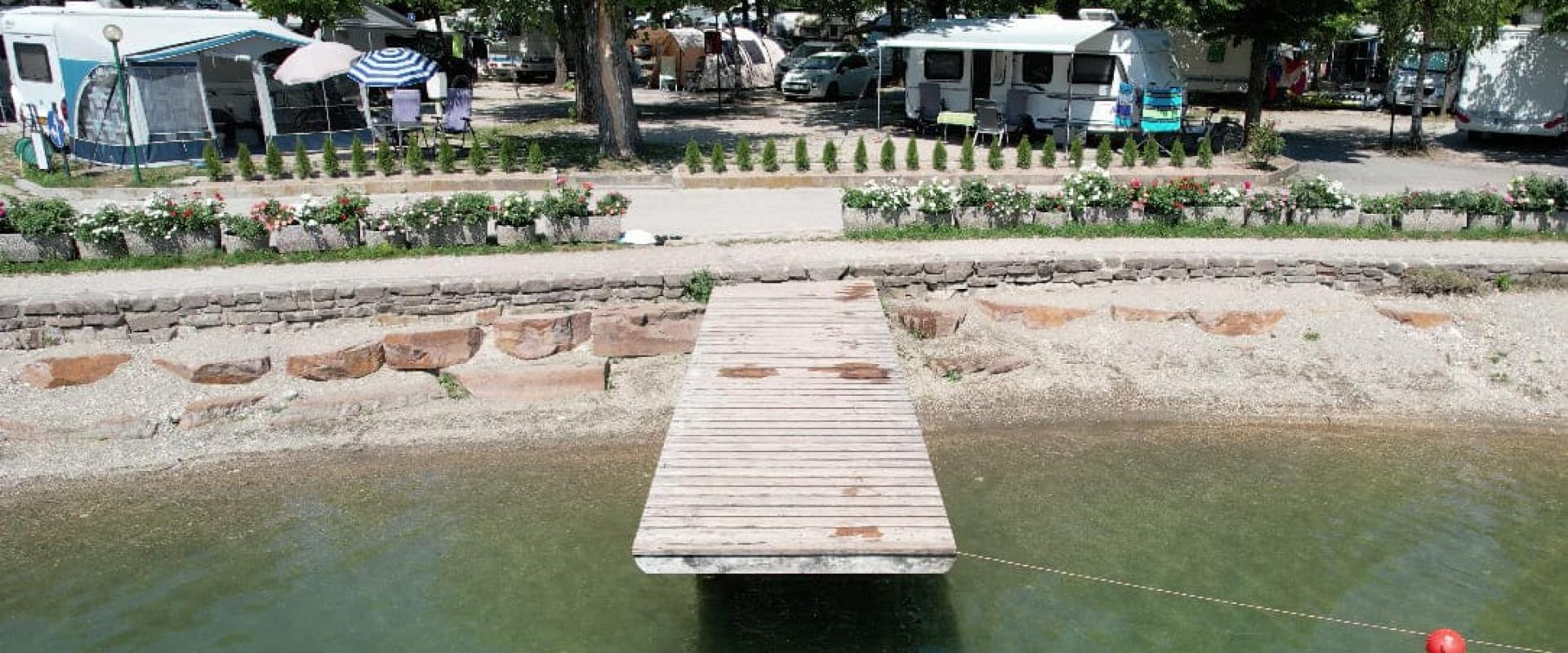 Campeggio con roulotte e molo di legno su un lago, circondato da alberi.