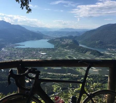 Vista panoramica su un lago con bicicletta in primo piano, circondato da montagne.