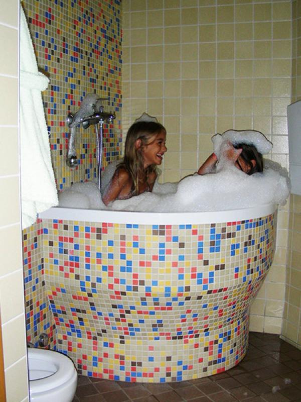 Due bambini ridono in una vasca da bagno con mosaico colorato, piena di schiuma.