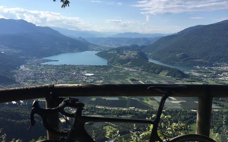 Vista panoramica su un lago e montagne, con una bicicletta in primo piano.