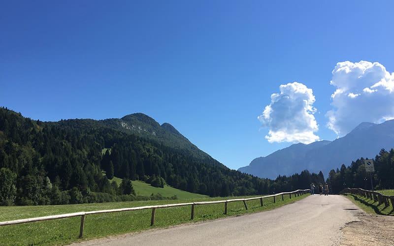 Strada di campagna con montagne, cielo blu e nuvole bianche.