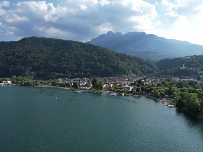 Panorama del lago con montagne sullo sfondo e un villaggio circondato da foreste.