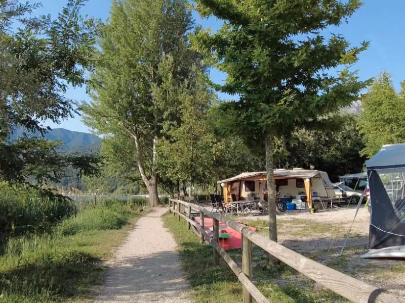 Sentiero in campeggio con roulotte e tende, circondato da alberi e natura.