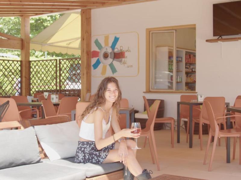 Donna sorridente beve vino in un caffè all'aperto con arredi moderni.
