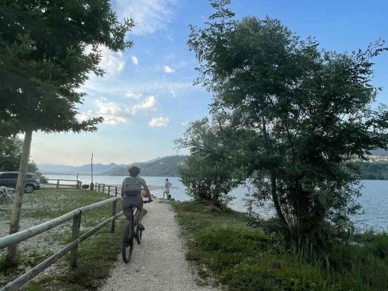 Persona in bici lungo un sentiero vicino a un lago, giornata serena.
