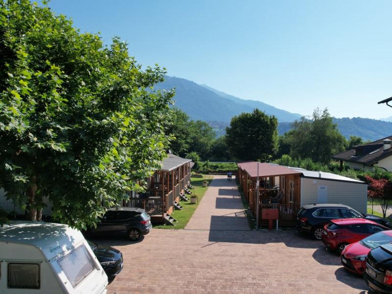 Campeggio con bungalow, auto parcheggiate e montagne sullo sfondo in una giornata soleggiata.