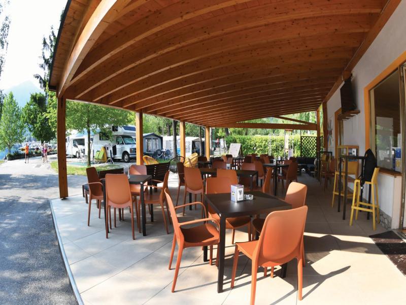 Terrazza coperta con tavoli e sedie, vista su camper e natura circostante.