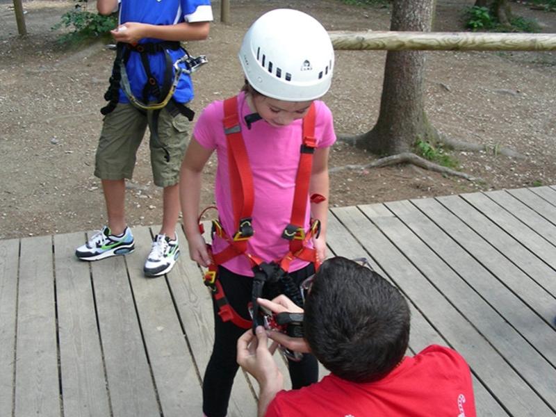 Bambina con casco e imbracatura controllata da un adulto in un parco avventura.