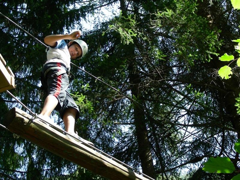 Bambino su percorso avventura tra gli alberi, indossa casco e imbracatura.