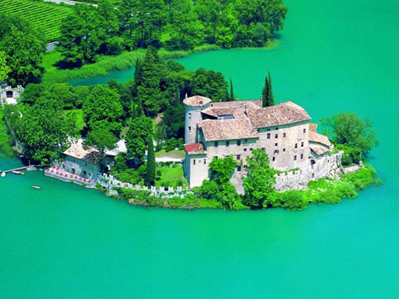 Castello su un'isola circondata da acque turchesi e vegetazione lussureggiante.