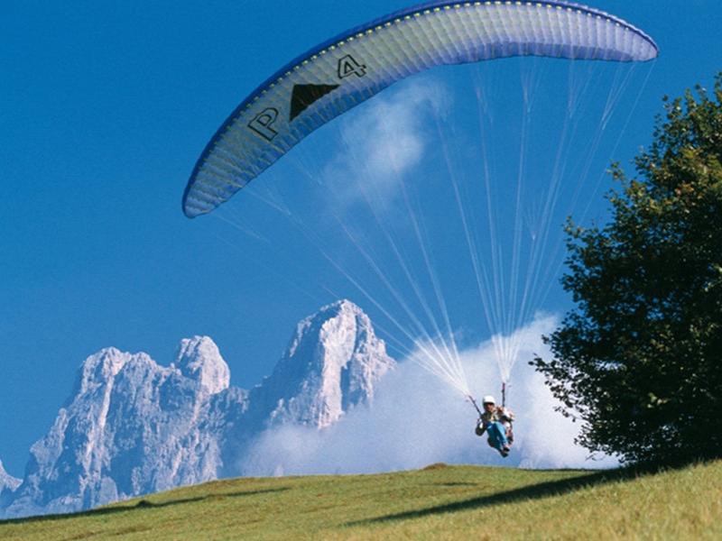 Parapendio in montagna con cielo azzurro e vette innevate sullo sfondo.