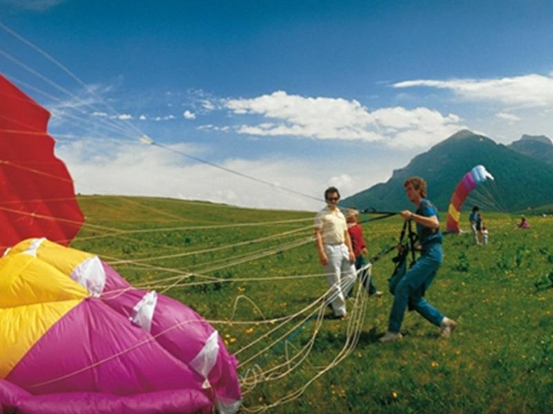Persone preparano un parapendio colorato in un prato montano, cielo sereno sopra.